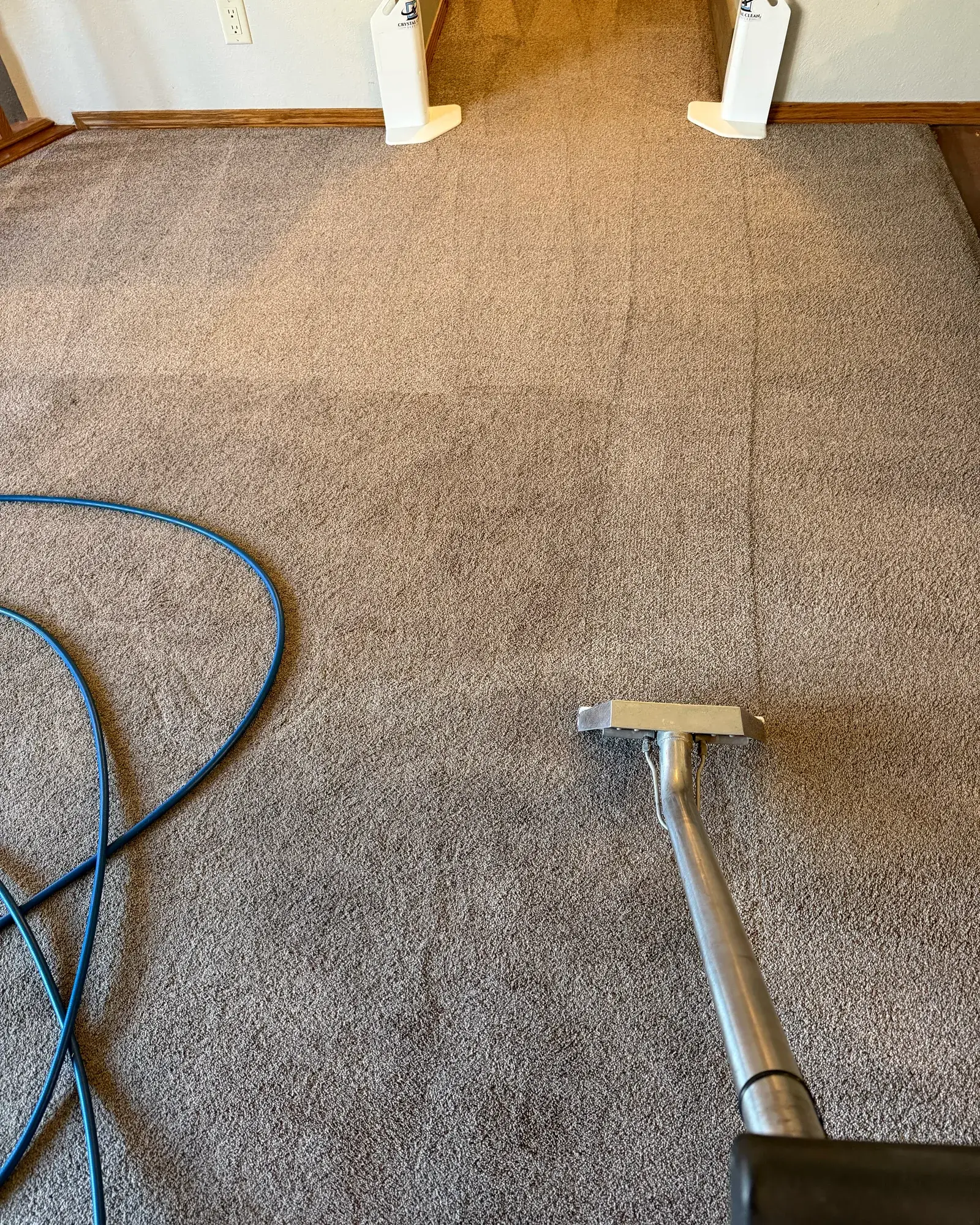 Carpet cleaning in progress in a Sioux Falls home — an extraction wand mid-pass, with Crystal Clean Services corner guards protecting the doorway.