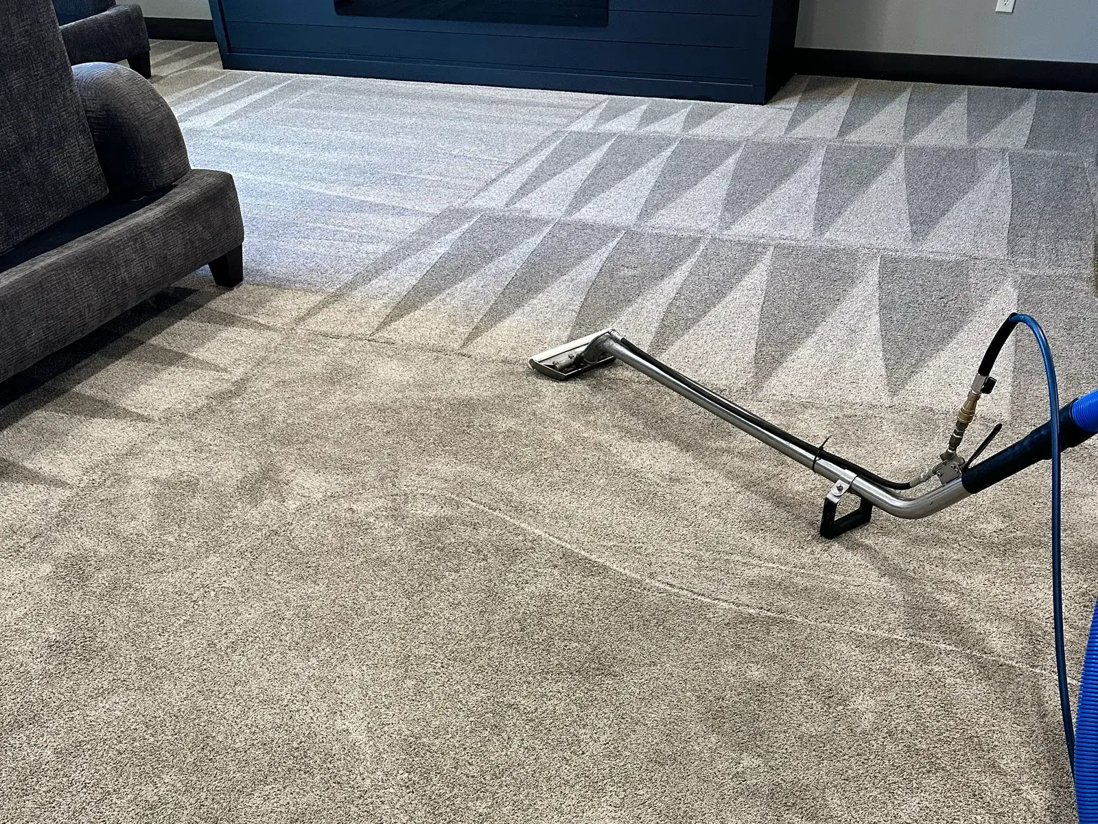 A hot-water extraction wand resting mid-pass on a commercial carpet, vacuum hose running back toward the machine.