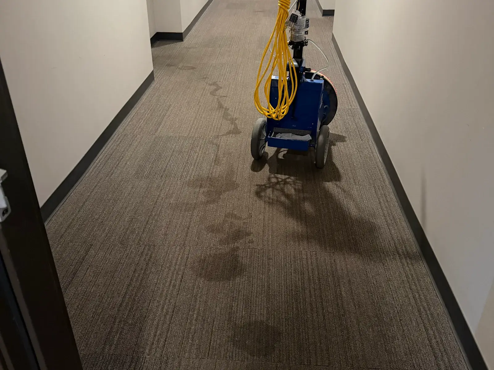A commercial corridor being cleaned, the machine parked mid-run on carpet tile.