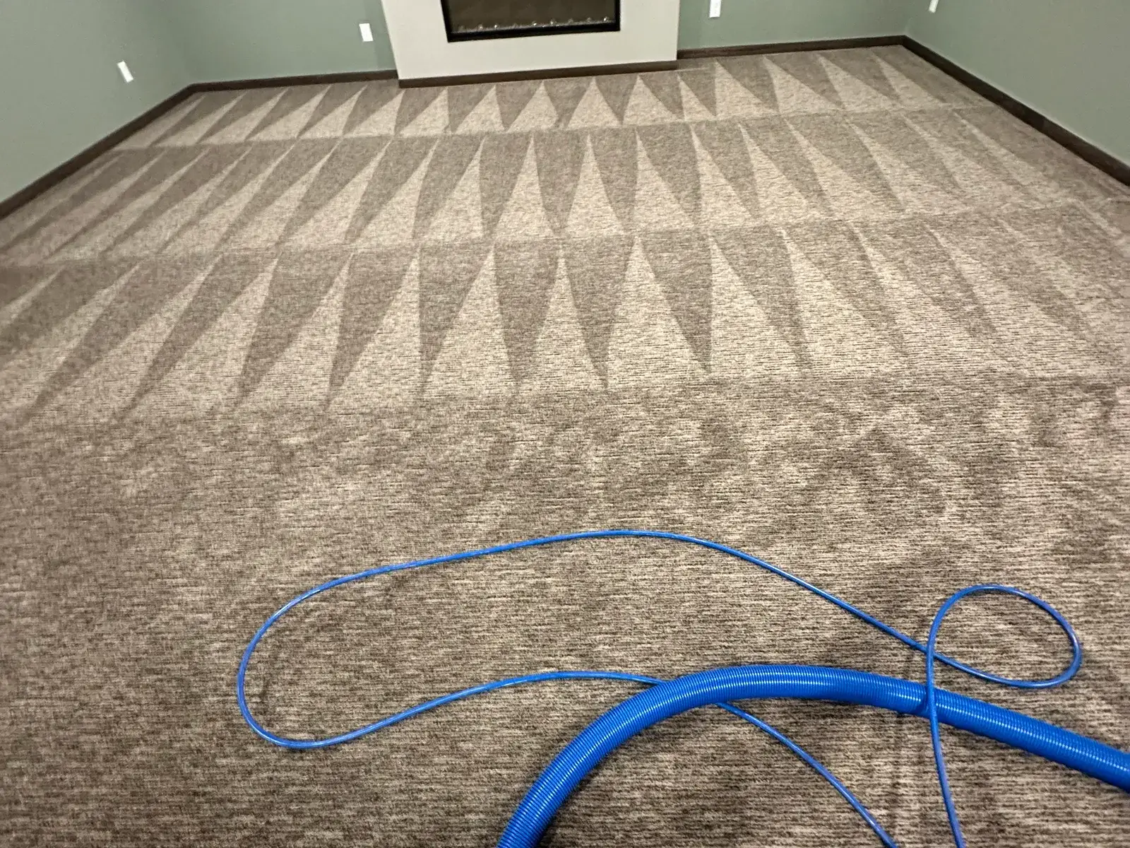 An empty room with patterned carpet part-way through cleaning, the cleaned area noticeably lighter than the rest.